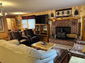Una sala de estar acogedora con chimenea, sillón de cuero, sofá blanco y estantería.