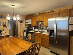 Una cocina con armarios de madera, un refrigerador de acero inoxidable, una mesa de comedor con sillas y una araña.