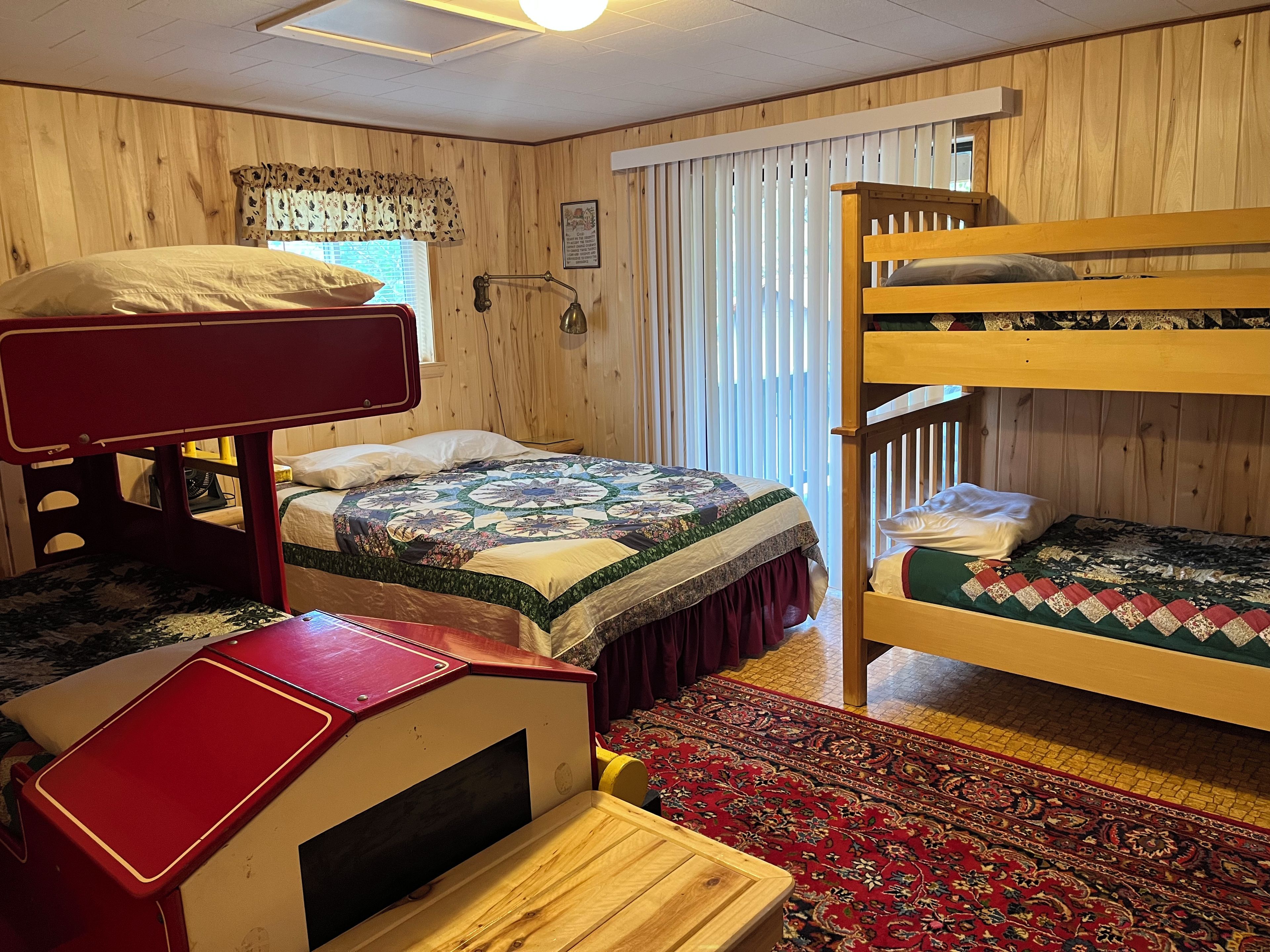 Ein Zimmer mit Etagenbett, Schreibtisch, gemustertem Teppich und Holzwänden.