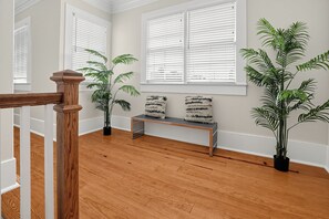 Quarto com piso de madeira, um banco e plantas em vasos.