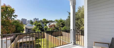 A covered balcony with a view of a backyard and neighboring houses.