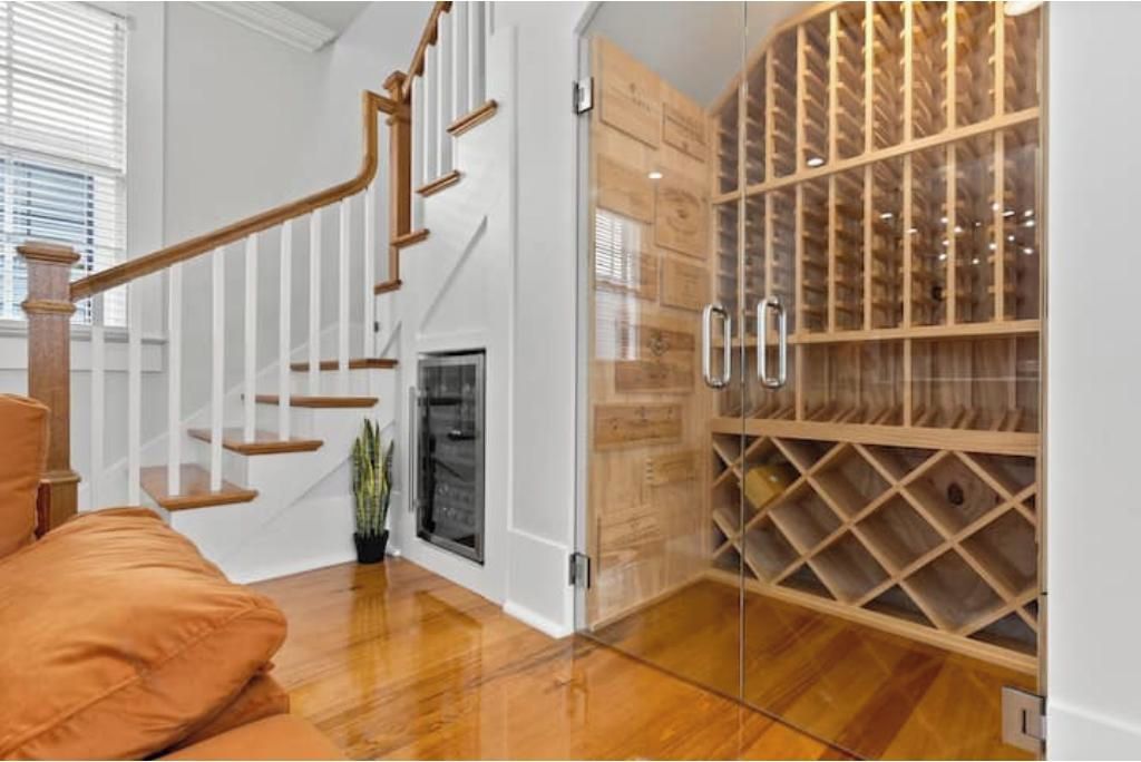 Un escalier avec des marches en bois et des rampes blanches, un meuble à vin en verre doté de plusieurs compartiments, et une plante en pot près de l’escalier.