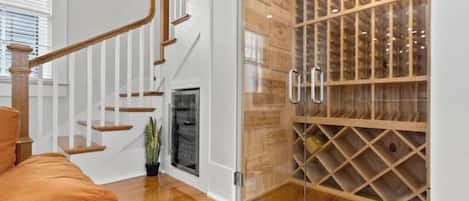 Un escalier avec des marches en bois et des rampes blanches, un meuble à vin en verre doté de plusieurs compartiments, et une plante en pot près de l’escalier.