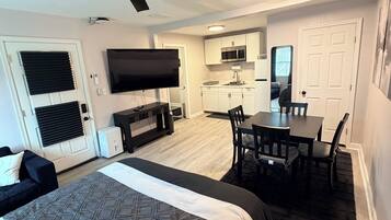 A compact hotel room with a bed, a desk, a chair, a television, and a kitchenette.