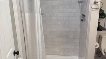 A shower area with a white curtain, a showerhead, and a tiled wall.