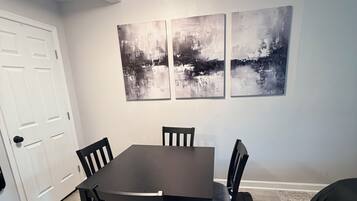 A dining area with a table and chairs, a black rug, and abstract wall art.