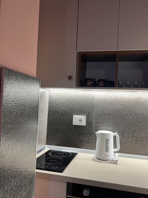 A kitchen with a black induction cooktop, a white electric kettle, and a cabinet with a textured backsplash.