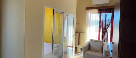 A room with a bed, a sofa, a round patterned rug, a sliding glass door, and an air conditioning unit.