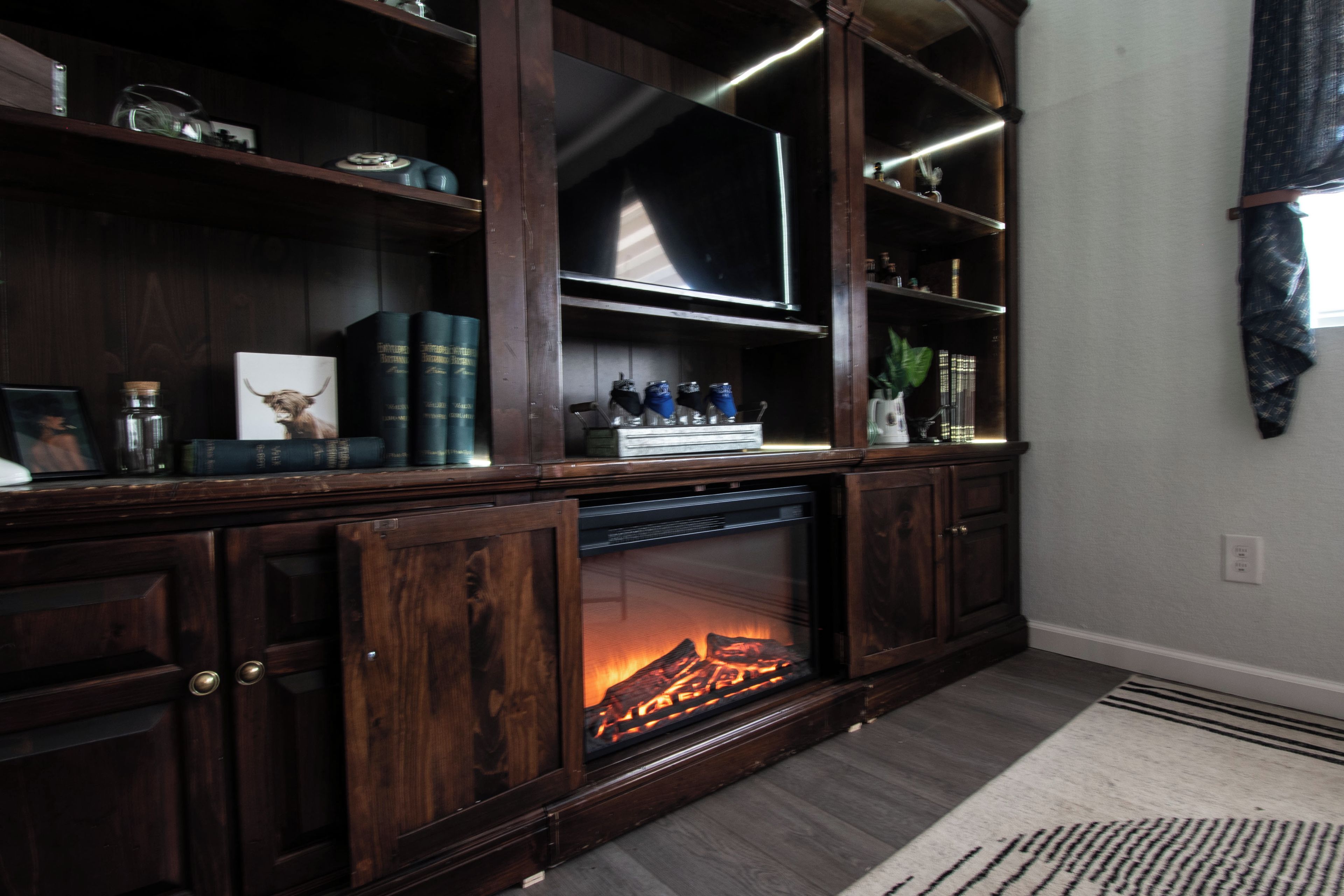 A wooden entertainment center with a fireplace, books, and decorative items.