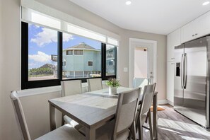 Eine moderne Küche mit einem eingebauten Edelstahlkühlschrank, einem Esstisch mit Stühlen und einem großen Fenster mit Blick auf ein Haus und den Himmel.