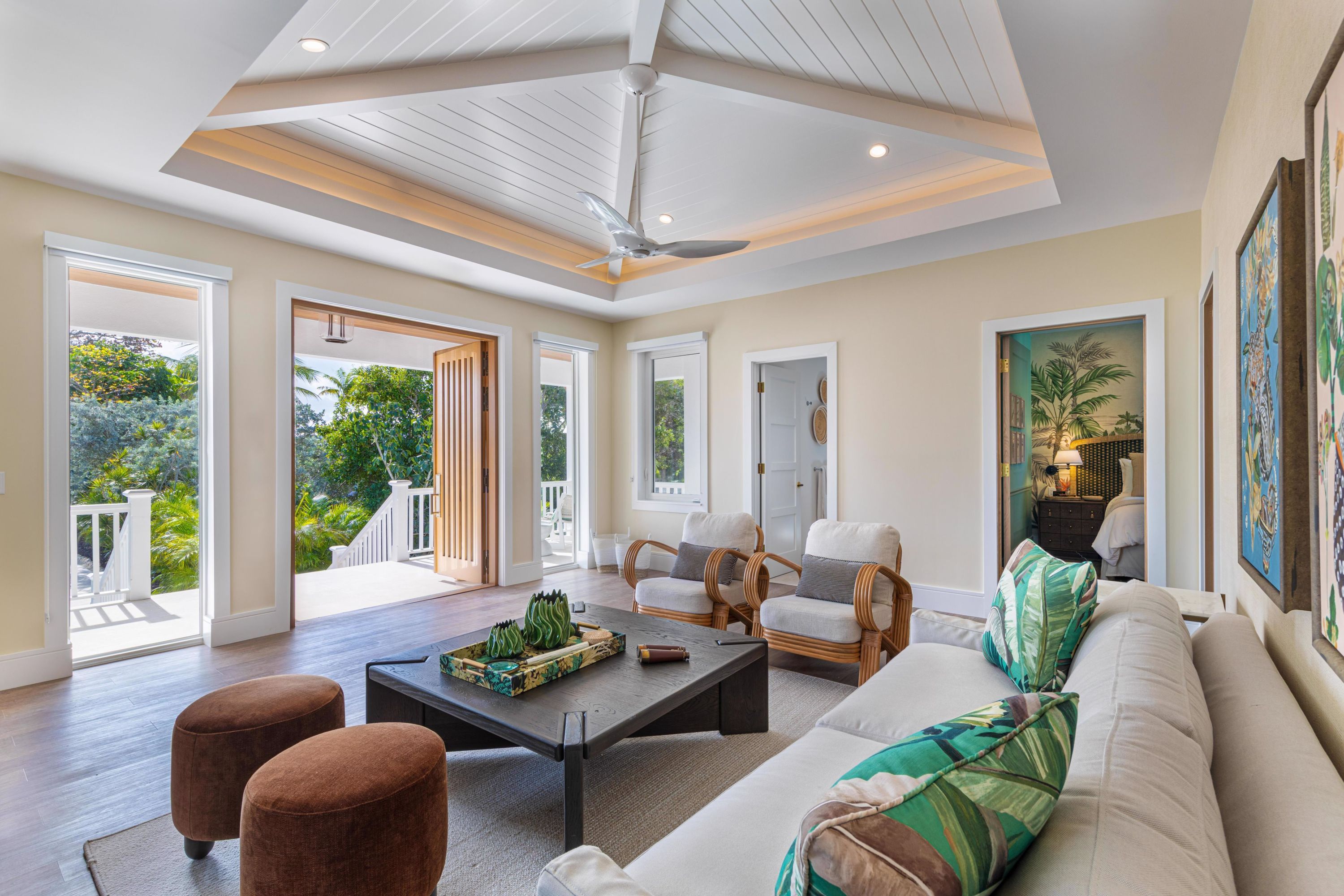 A spacious living room with a high ceiling, a ceiling fan, and a view of a lush garden through large windows.