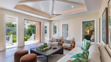 A spacious living room with a high ceiling, a ceiling fan, and a view of a lush garden through large windows.