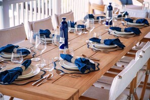A long dining table set with plates, glasses, and cutlery, with blue napkins and a bottle of water.