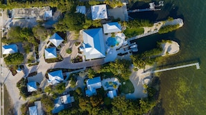 Vista aérea de um resort com vários edifícios, uma piscina e um cais que se estende sobre a água.