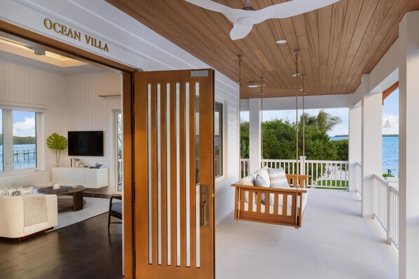 A modern living room with a TV, seating, and a view of the sea.