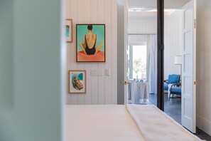 A hotel room with a bed, a painting of a person in a meditative pose, and a view of the outdoor seating area.