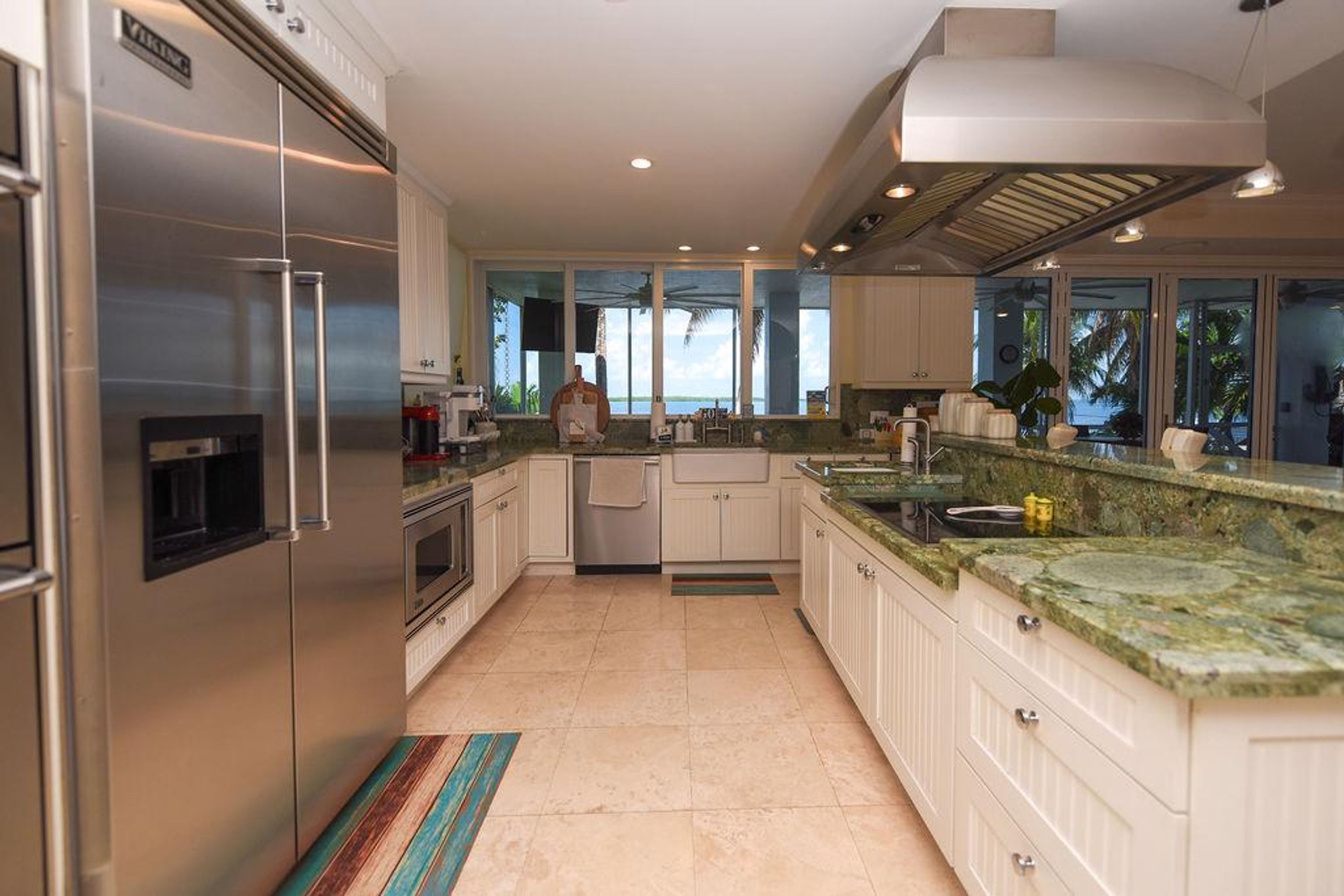 A modern kitchen with stainless steel appliances, a large island with a sink, and a view of the outdoors through the windows.
