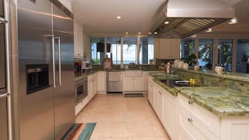 A modern kitchen with stainless steel appliances, a large island with a sink, and a view of the outdoors through the windows.