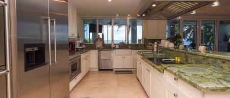 A modern kitchen with stainless steel appliances, a large island with a sink, and a view of the outdoors through the windows.