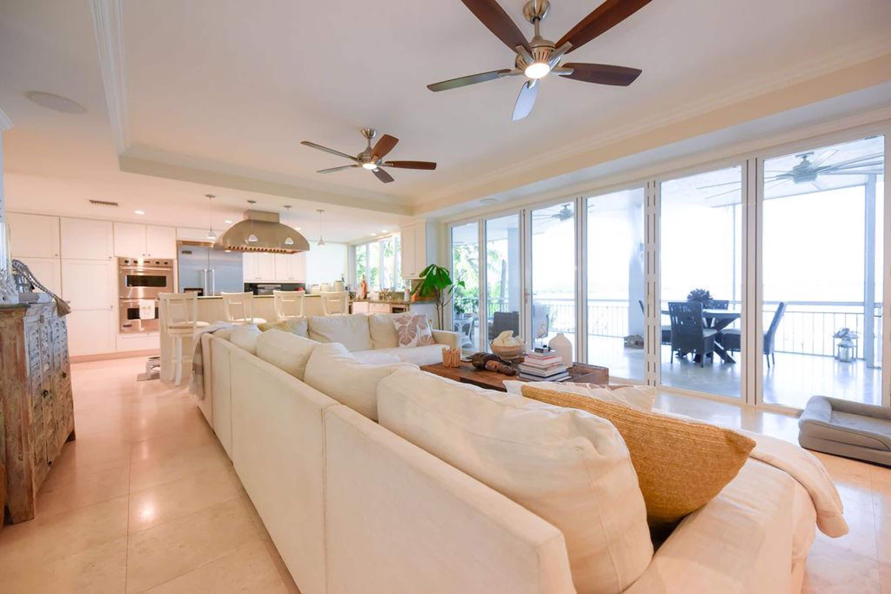 A spacious living area with a large white sofa, a dining table, and a kitchen in the background.