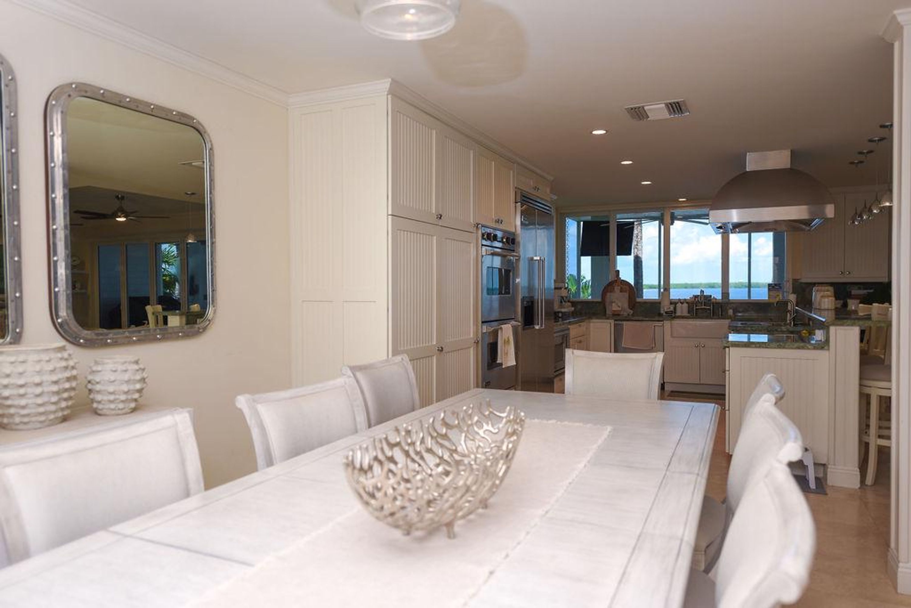 A spacious dining area with a large table, white chairs, and a decorative bowl centerpiece.