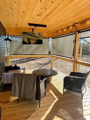 Un espace extérieur abrité, aménagé avec une table, des chaises et un écran de télévision.