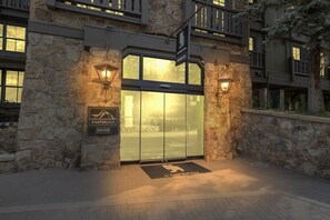 A hotel entrance with a stone facade, a glass door, and two wall-mounted lanterns. - 2-Bedroom Condo at Gravity Haus (Vail)