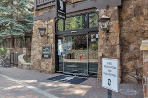 A building entrance with a sign for guest registration and valet parking, a stone facade, and a doormat with a logo. - 2-Bedroom Condo at Gravity Haus (Vail)