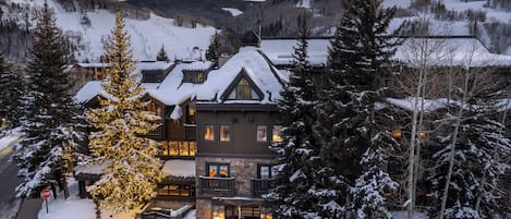 A lodge with a snow-covered roof, multiple windows, and a prominent Christmas tree with lights.