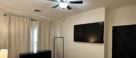 A bedroom with a bed, a ceiling fan, a TV mounted on the wall, and a door.