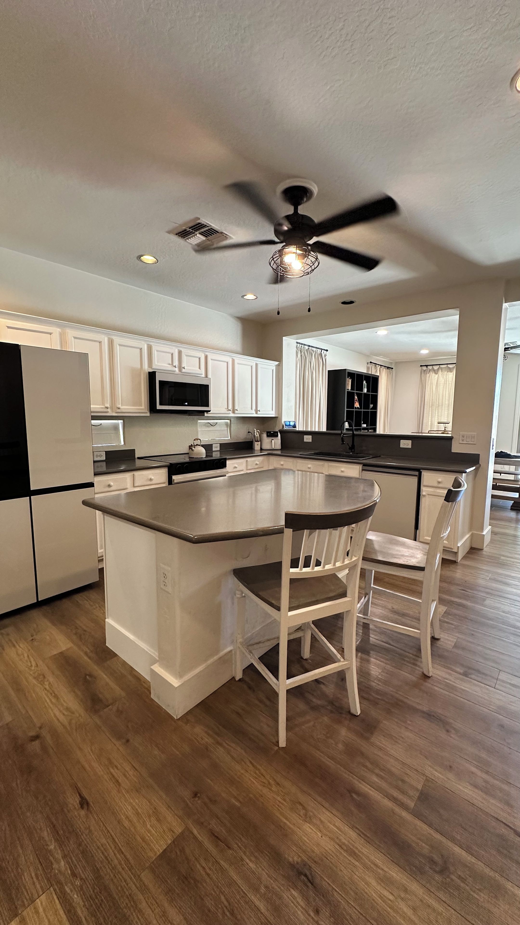 A modern kitchen with white cabinetry, a central island with bar stools, and a ceiling fan.