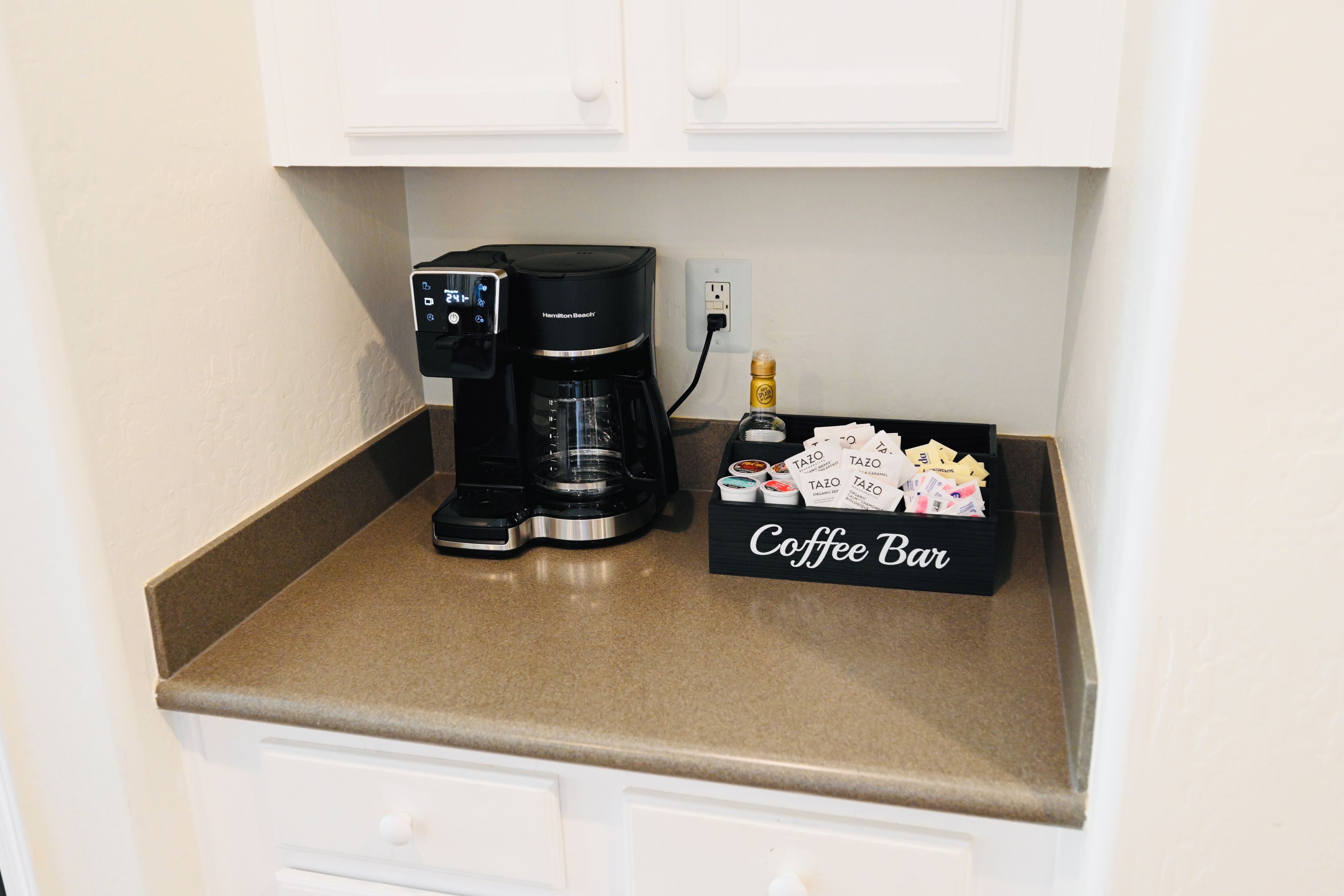 A coffee station with a Hamilton Beach coffee maker, a Tazo tea dispenser, and a coffee bar sign.