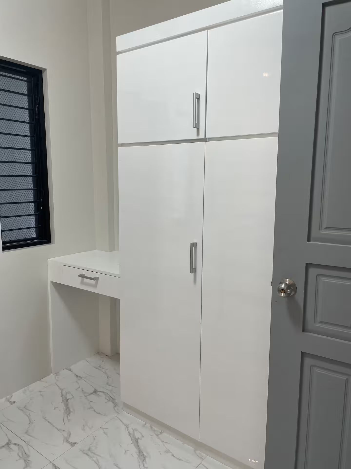 A room with a white wardrobe, a small shelf, and a door.