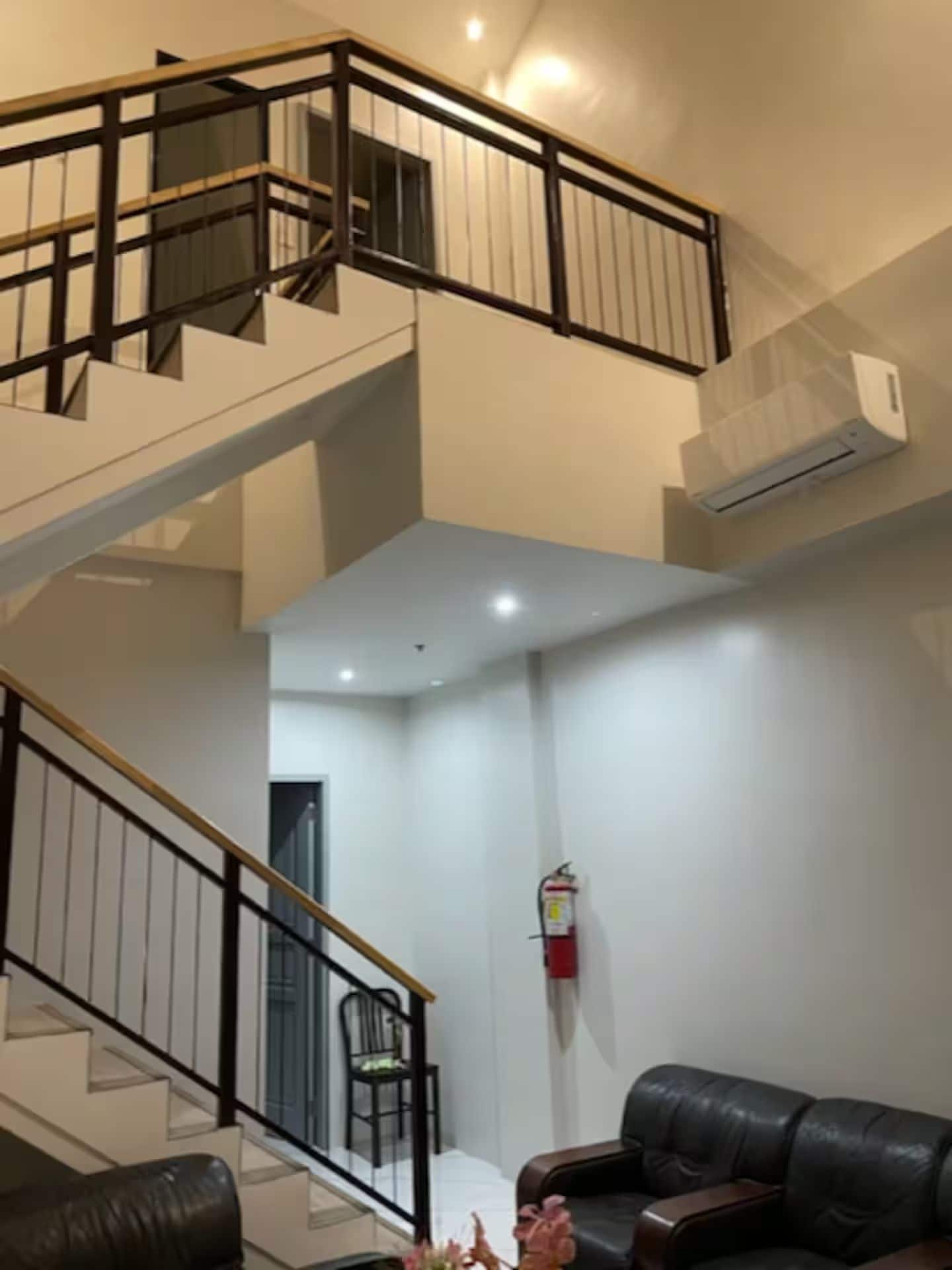 A multi-level interior with a staircase, a fire extinguisher, and a leather sofa.