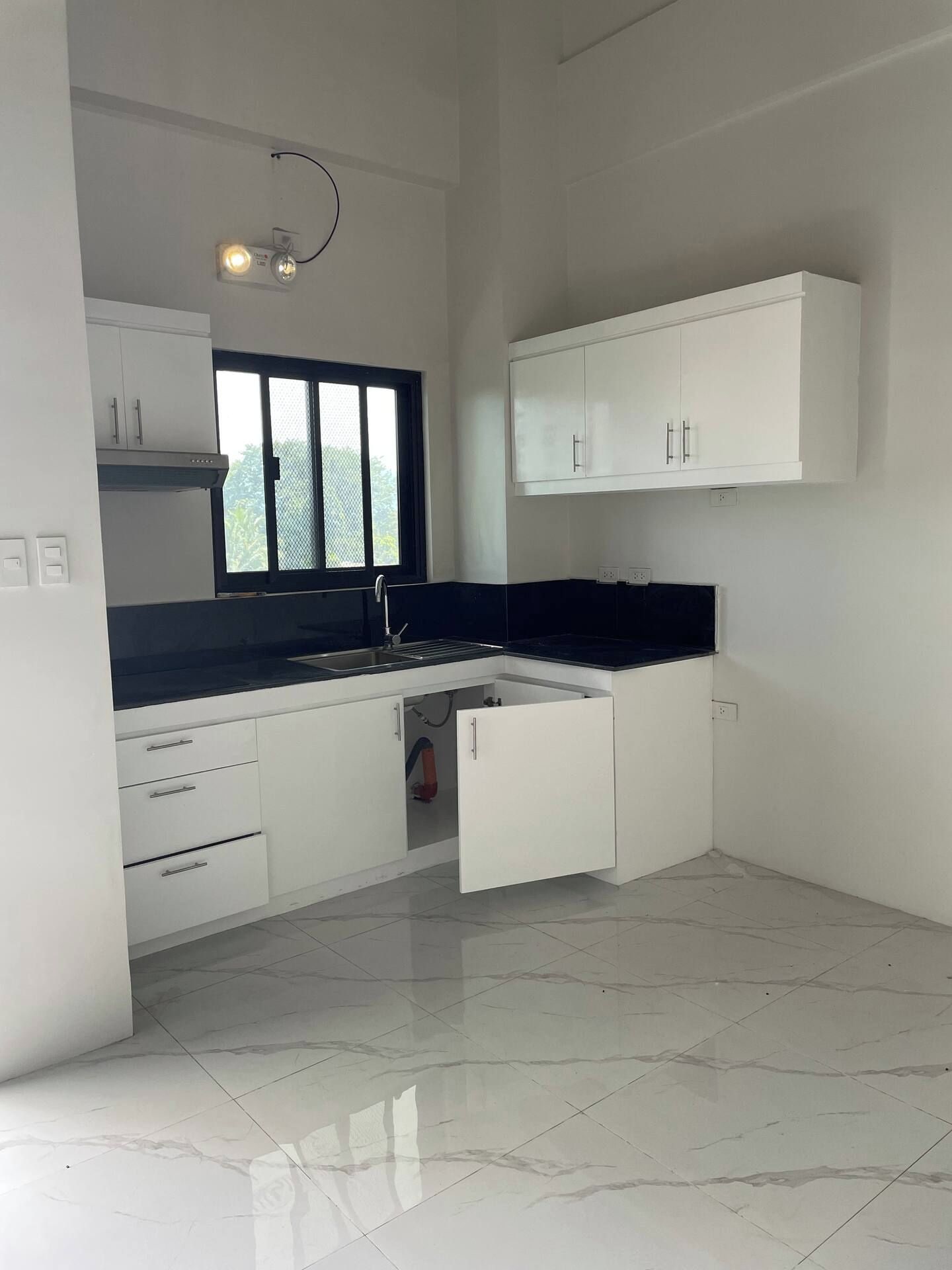 A modern kitchen with white cabinetry, a black countertop, and a window with a view.