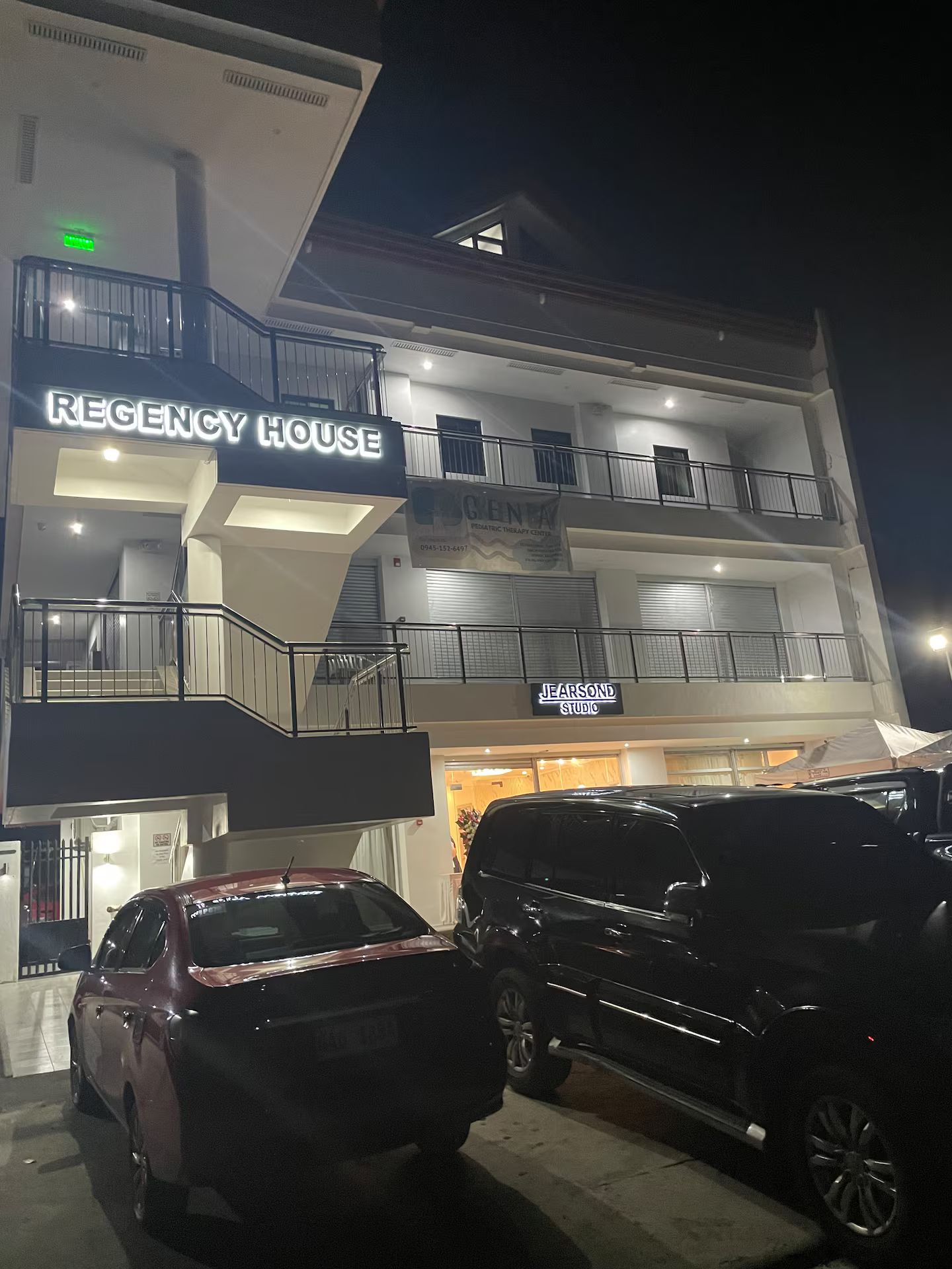 Ein mehrstöckiges Gebäude mit der Beschriftung 'REGENCY HOUSE' und 'JEARSOND STUDIO' im Erdgeschoss. Vor dem Gebäude befinden sich zwei parkende Autos.