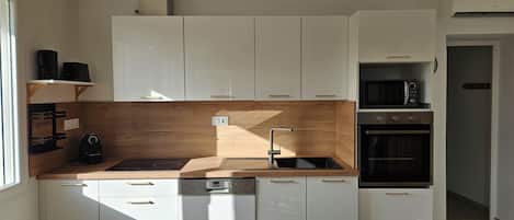 Una cocina moderna con armarios blancos, protector contra salpicaduras de madera y electrodomésticos integrados, incluyendo lavavajillas, microondas y horno.