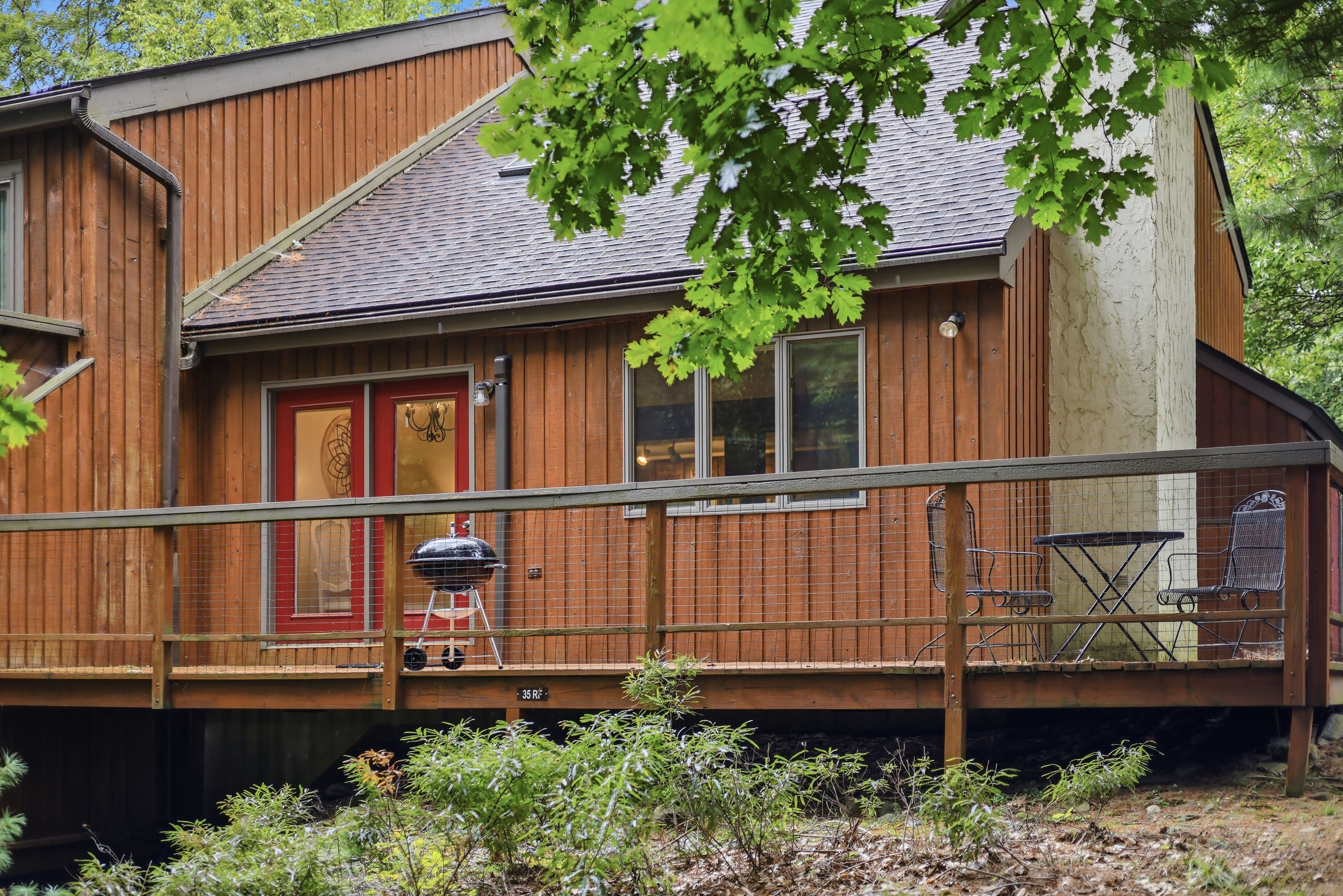 A wooden cabin with a covered deck, a grill, and outdoor seating.