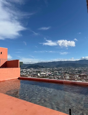 A rooftop pool with a clear view of a cityscape and mountains in the distance.