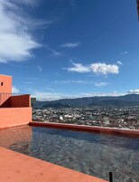A rooftop pool with a clear view of a cityscape and mountains in the distance.