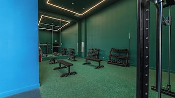 Ett gym med gröna väggar, speglar i taket och olika typer av träningsutrustning.
