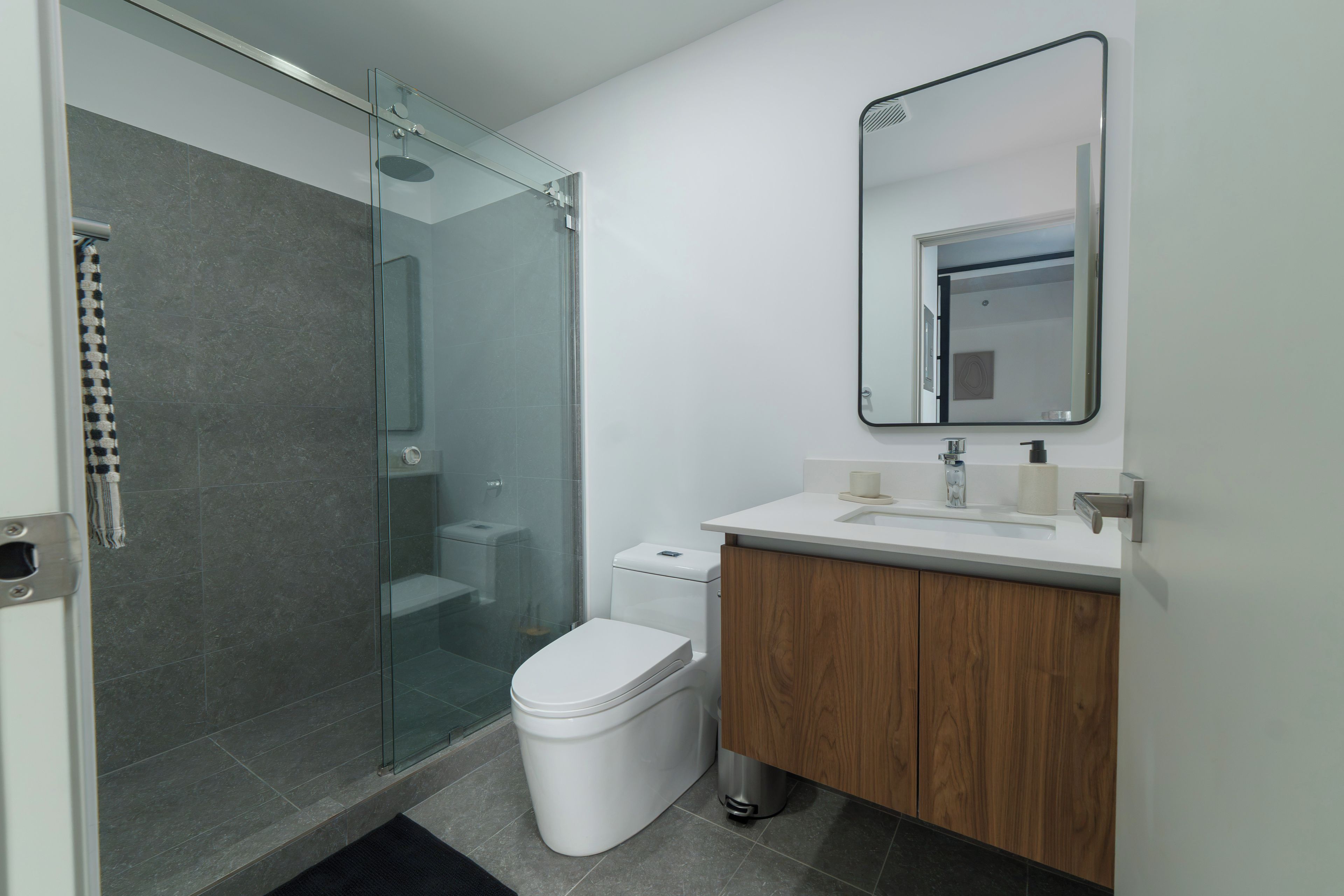 Un baño moderno con cabina de ducha de vidrio, inodoro blanco y tocador de madera con espejo.