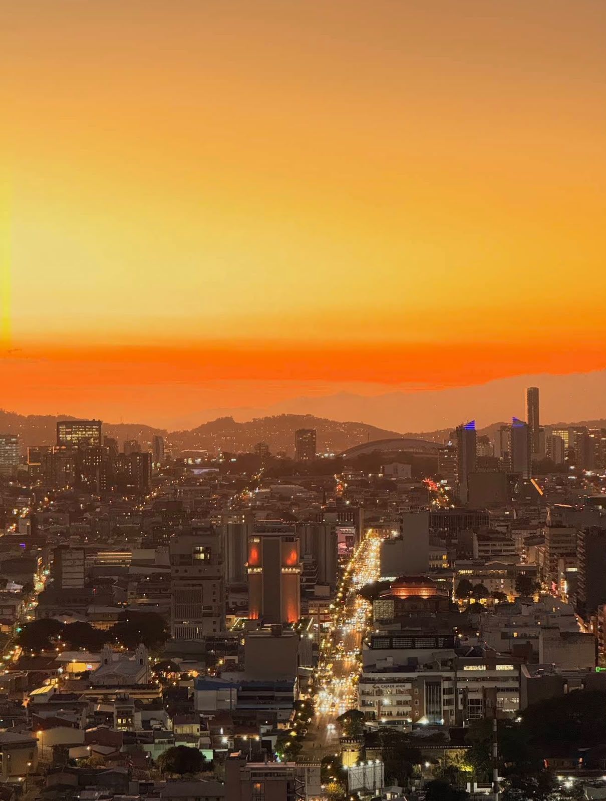 Paisagem urbana ao entardecer, com uma avenida principal cortando o centro.