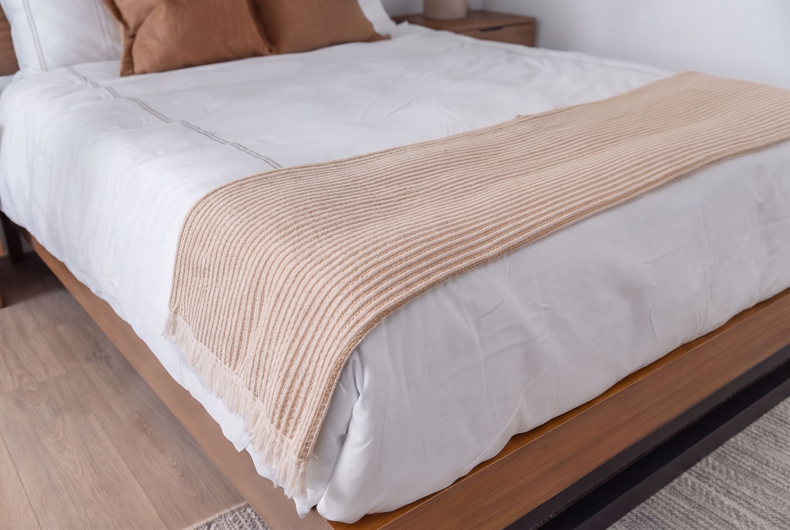 Una cama con colchón blanco, manta color beige y cabecera de madera.