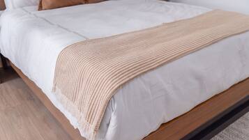 Una cama con colchón blanco, manta color beige y cabecera de madera.