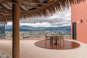 A terrace with a view of a cityscape and mountains, featuring a round wooden table and chairs.