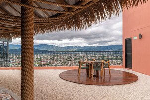Una terraza con vistas a un paisaje urbano y montañas, que incluye una mesa y sillas de madera redonda.