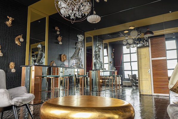 A modern interior with a reflective floor, a central gold table, and a chandelier.