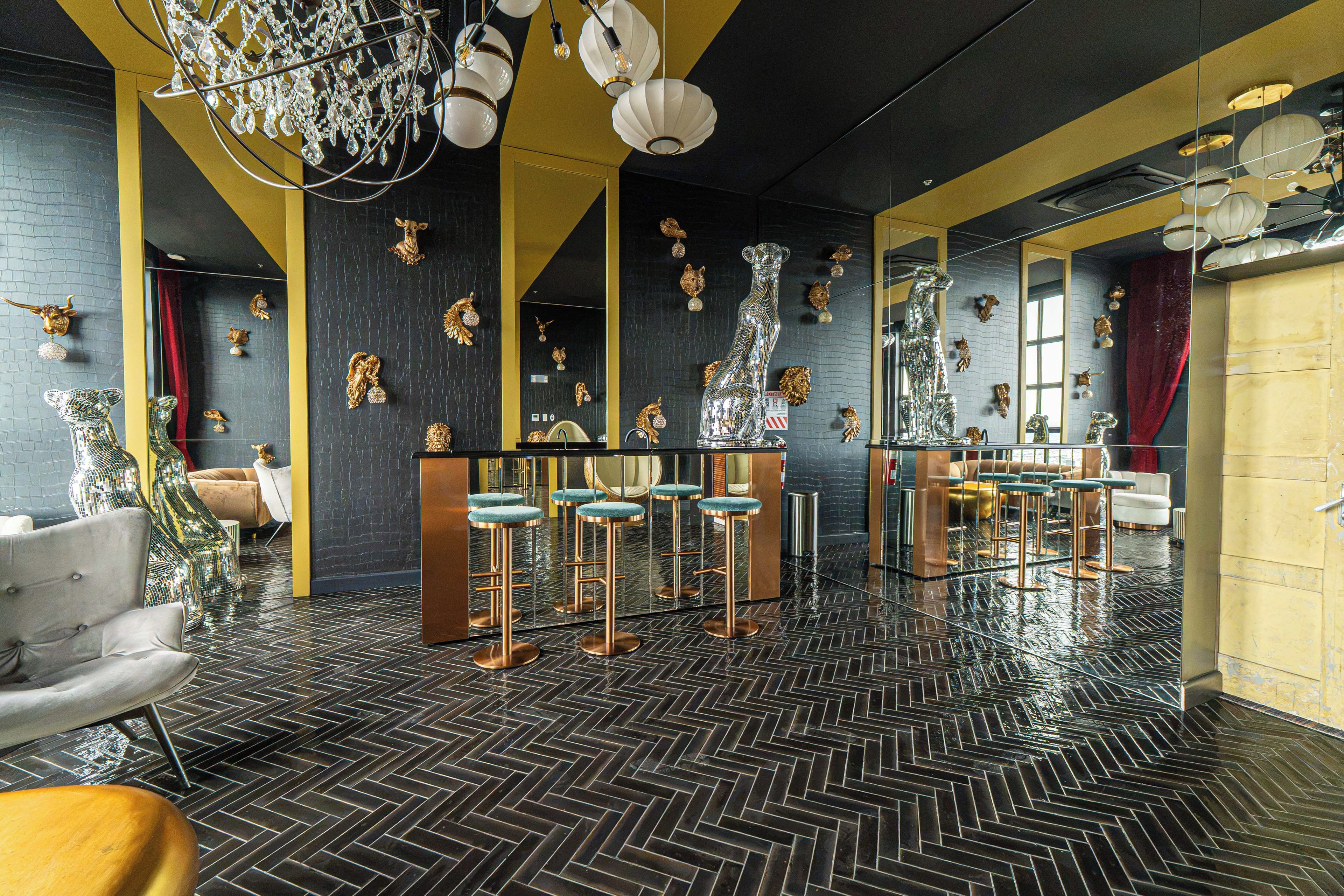 A bar area with mirrored bar stools, a large mirror, and decorative wall art.