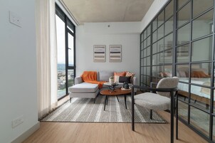 A modern living room with a sofa, armchair, coffee table, and a view through large windows.